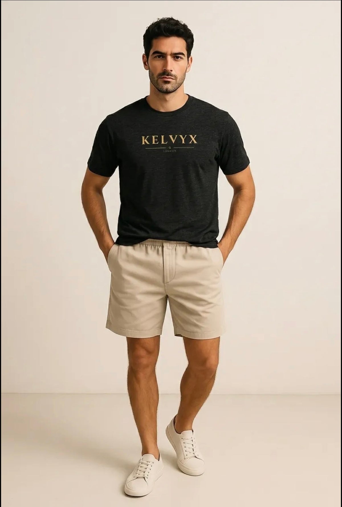 A man modeling a black short-sleeve t-shirt with 'KELVYX' printed in gold across the chest, paired with beige shorts and white sneakers, against a plain beige studio background.